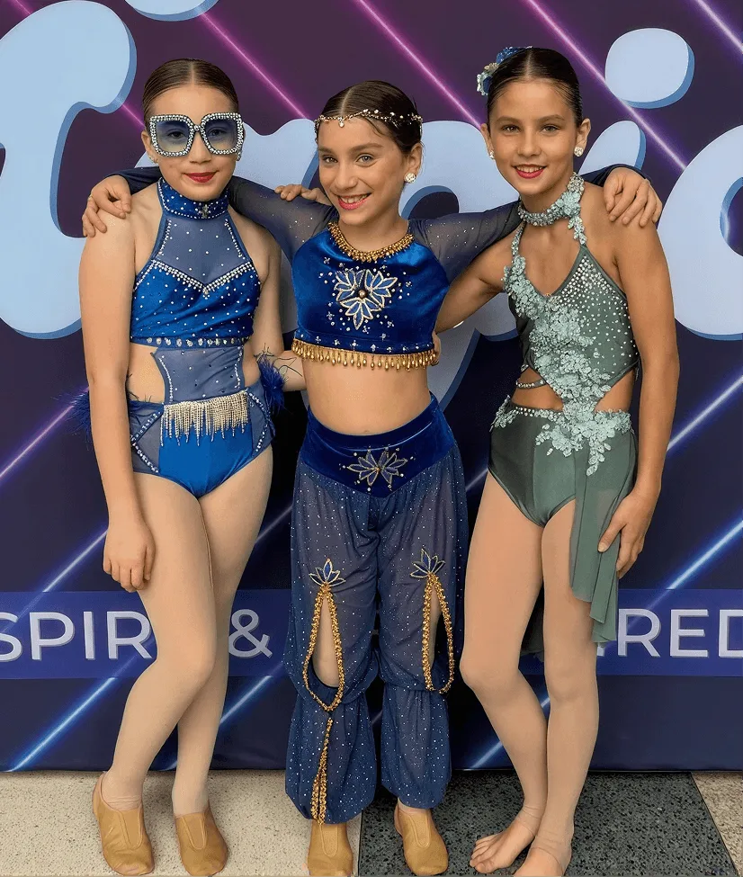 Three Momentum dancers in blue costumes smiling together at a dance competition