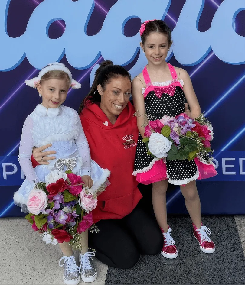 A Momentum instructor with two young dancers holding flowers after a recital